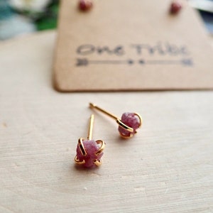 May include: A pair of gold stud earrings with pink, raw, crystal-like stones set in a gold wire cage.
