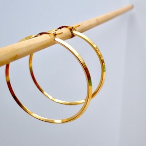 May include: A pair of gold hoop earrings. The earrings are large and have a simple, elegant design.
