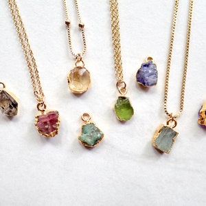 May include: A set of nine gold necklaces featuring various coloured gemstone pendants. The pendants are all rough-cut and have a natural, organic appearance. The necklaces are ideal for layering or wearing individually.