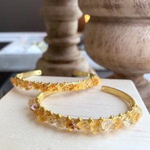 Op de afbeelding: Twee gouden armbanden met een rij kleine, gefacetteerde, oranje-bruine edelstenen. De armbanden liggen op elkaar.
