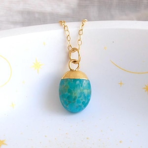Peut inclure: Un collier &agrave; cha&icirc;ne dor&eacute;e avec un pendentif turquoise. Le pendentif est de forme ovale avec un capuchon dor&eacute;. La pierre turquoise pr&eacute;sente un motif mouchet&eacute; et est d'un bleu-vert vif. Le collier est pr&eacute;sent&eacute; sur une surface blanche.