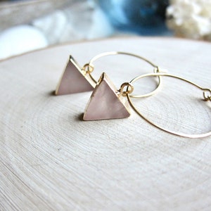 May include: A pair of gold hoop earrings with pink triangle-shaped charms. The charms have a pearlescent finish.