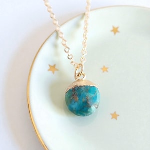Peut inclure: Un collier &agrave; cha&icirc;ne dor&eacute;e avec un pendentif rond turquoise. Le pendentif est coiff&eacute; d'un capuchon dor&eacute; et repose sur une assiette vert clair orn&eacute;e d'&eacute;toiles dor&eacute;es. Bijou.