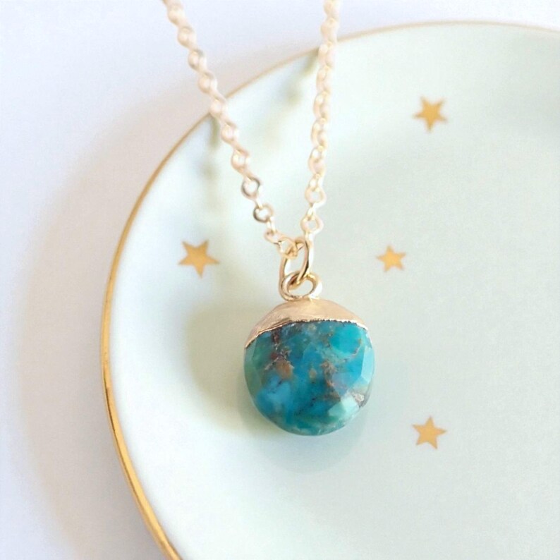 Peut inclure: Un collier &agrave; cha&icirc;ne dor&eacute;e avec un pendentif rond turquoise. Le pendentif est coiff&eacute; d'un capuchon dor&eacute; et repose sur une assiette vert clair orn&eacute;e d'&eacute;toiles dor&eacute;es. Bijou.