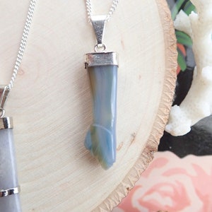 May include: A silver chain necklace with a pendant made of a light blue and gray agate stone. The stone is shaped like a long, thin point.