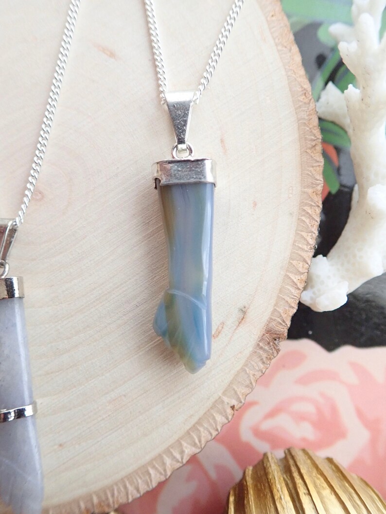 May include: A silver chain necklace with a pendant made of a light blue and gray agate stone. The stone is shaped like a long, thin point.
