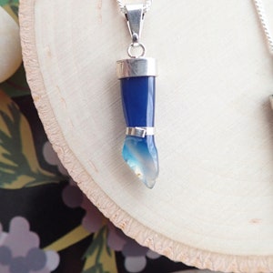 May include: A silver chain necklace with a blue agate pendant shaped like a hand. The pendant is set in silver and has a gradient of blue to white.