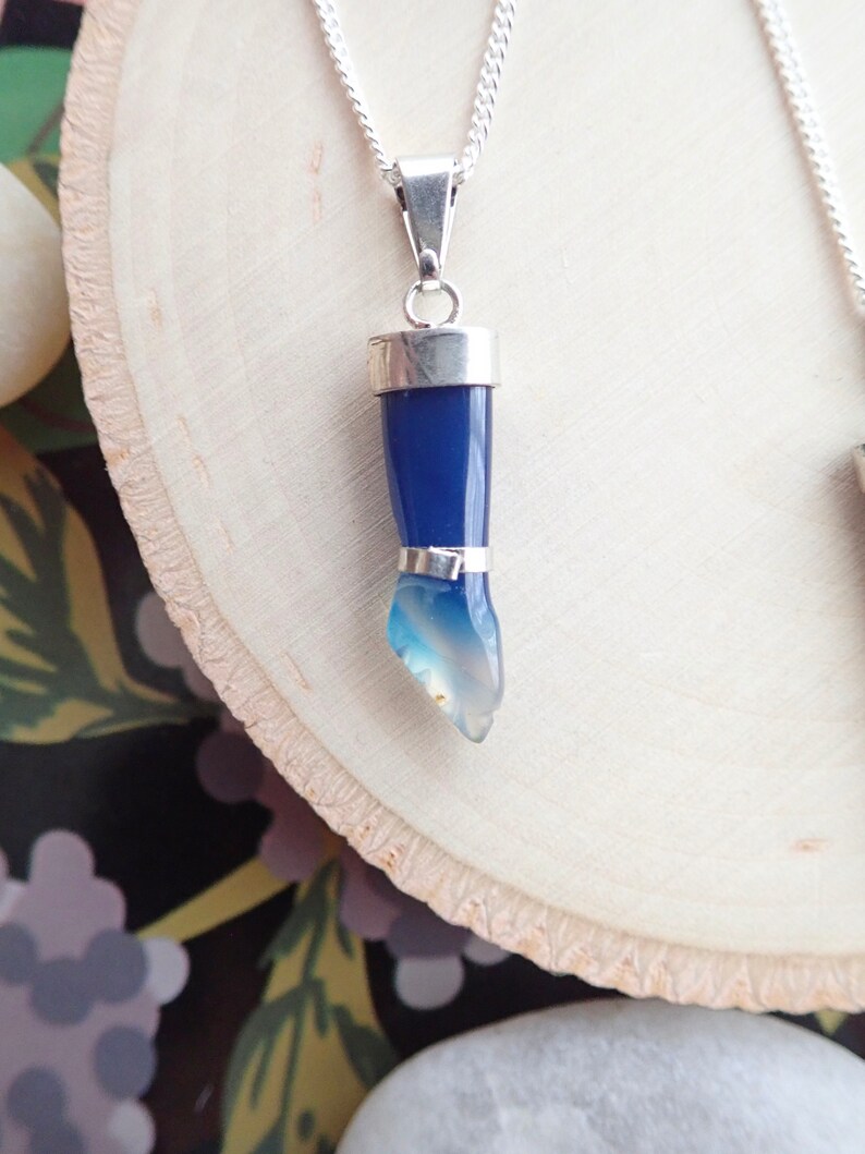 May include: A silver chain necklace with a blue agate pendant shaped like a hand. The pendant is set in silver and has a gradient of blue to white.
