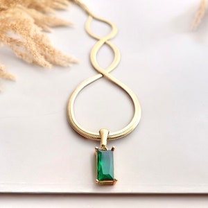 May include: A gold chain necklace with a green gemstone pendant. The chain is a snake chain style and the pendant is a rectangular emerald cut.