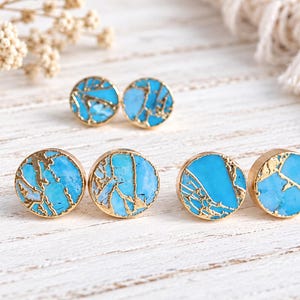 May include: Three pairs of circular stud earrings featuring a bright turquoise stone inlay with intricate gold-coloured veining. Each earring has a smooth, polished gold-toned metal rim surrounding the vibrant blue and gold patterned stone surface.