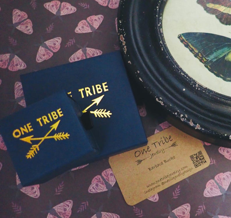 Peut inclure: Deux bo&icirc;tes &agrave; bijoux bleu marine avec des lettres dor&eacute;es indiquant "ONE TRIBE" et "TRIBE". Une petite carte de visite est &eacute;galement pr&eacute;sente. L'arri&egrave;re-plan pr&eacute;sente un motif r&eacute;p&eacute;titif de papillons roses.