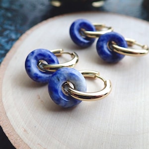 May include: A pair of gold hoop earrings with blue and white stone accents. The stone is a round shape and has a marbled pattern.
