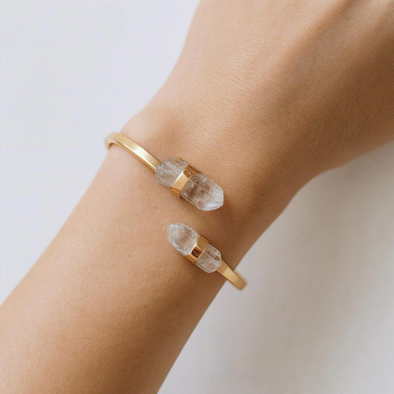 May include: Gold-tone open cuff bracelet featuring two clear quartz crystal accents. The crystals are held in place with gold bands. This elegant bracelet is a stylish accessory.