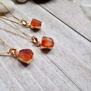 May include: Three gold necklaces with carnelian stone pendants. The carnelian stones are rough and natural, with a reddish-orange color.
