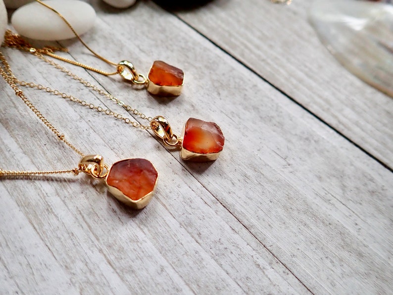 May include: Three gold necklaces with carnelian stone pendants. The carnelian stones are rough and natural, with a reddish-orange color.
