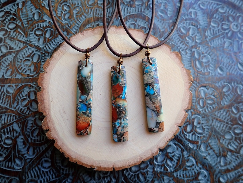 May include: Three necklaces with brown leather cords and rectangular pendants made of colourful, multi-coloured, and patterned stone.