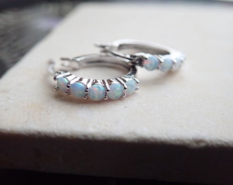 May include: A pair of silver hoop earrings with a row of white opals set in each hoop.