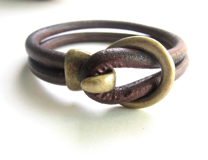 May include: A brown leather bracelet with a brass clasp. The bracelet is double-layered and has a knotted design.