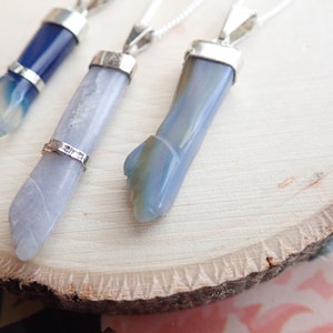 May include: Three silver pendants with blue agate stones. The stones are all different shapes and sizes. The pendants are hanging from silver chains.