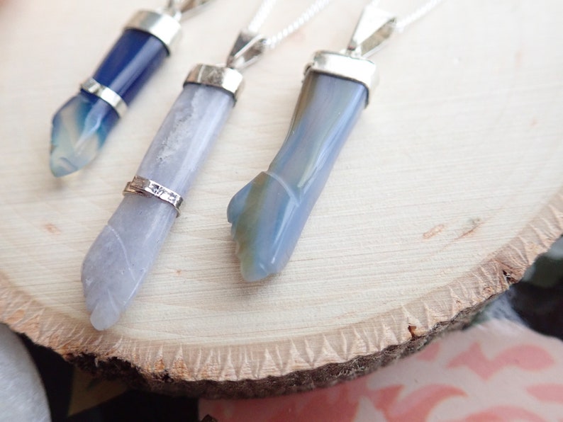 May include: Three silver pendants with blue agate stones. The stones are all different shapes and sizes. The pendants are hanging from silver chains.