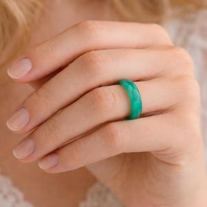 May include: A smooth, solid band ring in a vibrant, translucent emerald green color. The ring features a polished finish with subtle internal variations in tone, creating a marbled effect throughout the circular band worn on a finger.