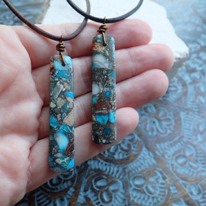 May include: Two necklaces with brown leather cords and long, rectangular pendants made of blue, brown, and white marbled stone.