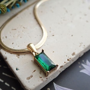 Peut inclure: Un collier en chaîne dorée avec un pendentif en forme d'émeraude verte.
