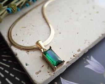 May include: A gold chain necklace with a green emerald-shaped pendant.