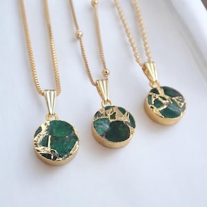 May include: Three gold-colored necklaces with round, green pendants. The pendants have a gold-colored, textured border and a green, stone-like center. The necklaces are displayed on a white surface.