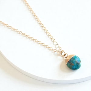 Peut inclure: Un collier &agrave; cha&icirc;ne dor&eacute;e avec un pendentif turquoise et or. Le pendentif est une pierre arrondie avec un capuchon dor&eacute;, pr&eacute;sentant un m&eacute;lange de teintes bleues et vertes. Le collier est pr&eacute;sent&eacute; sur une surface blanche.