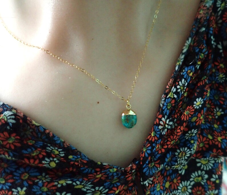 Peut inclure: Un collier dor&eacute; avec un petit pendentif turquoise. Le pendentif est orn&eacute; d'un capuchon dor&eacute;. Le collier est port&eacute; sur un haut &agrave; motifs floraux.