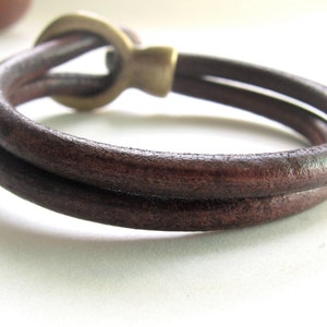 May include: A brown leather bracelet with a brass clasp. The bracelet is double-layered and has a simple design.
