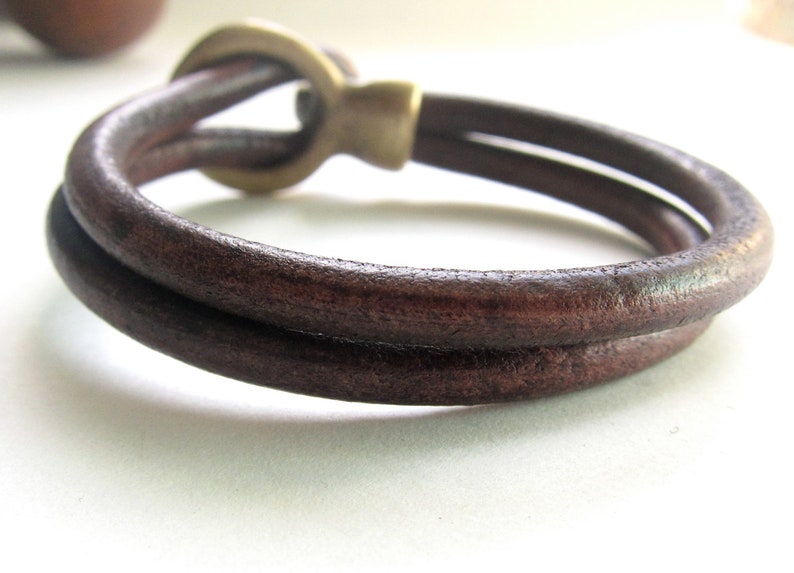May include: A brown leather bracelet with a brass clasp. The bracelet is double-layered and has a simple design.