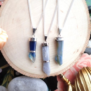 May include: Three silver necklaces with blue and gray agate stone pendants in the shape of a hand. The pendants are all different shades of blue and gray.