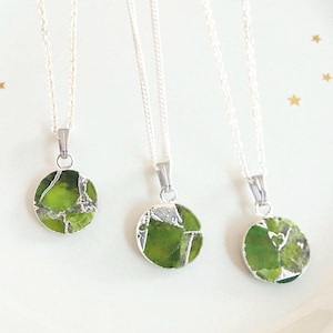 May include: Three silver necklaces with round, green stone pendants. The pendants have a silver border and are suspended from delicate silver chains. The necklaces are displayed on a white plate with gold star accents.