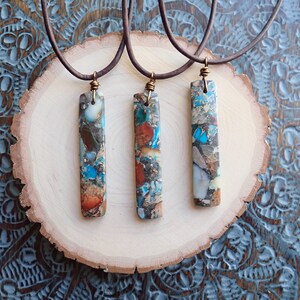 May include: Three necklaces with brown leather cords and rectangular pendants made of colourful, multi-coloured, and patterned stone.