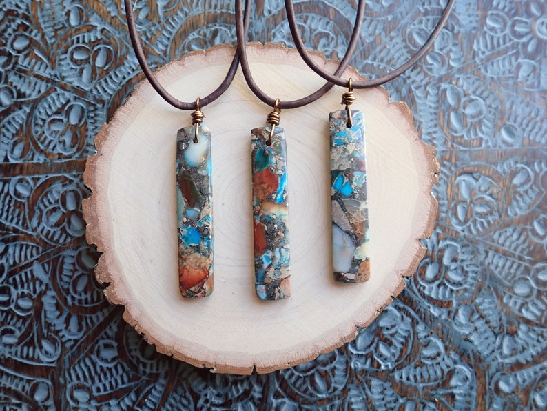 May include: Three necklaces with brown leather cords and rectangular pendants made of colourful, multi-coloured, and patterned stone.