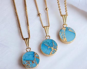 May include: Three gold-coloured necklaces with round, light blue pendants. The pendants have a gold-coloured, cracked-stone design. The necklaces are displayed on a white surface.