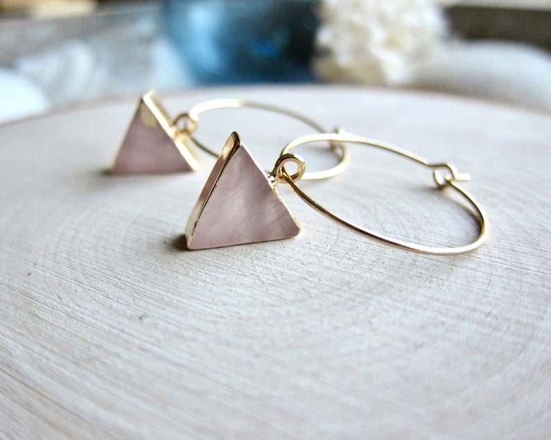 May include: A pair of gold hoop earrings with a pink triangle pendant on each hoop.