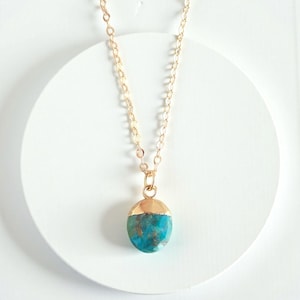 Peut inclure: Un collier &agrave; cha&icirc;ne dor&eacute;e avec un pendentif turquoise et or. Le pendentif de forme ovale pr&eacute;sente une pierre turquoise vibrante avec du m&eacute;tal dor&eacute; recouvrant la moiti&eacute; sup&eacute;rieure. Le collier est pr&eacute;sent&eacute; sur une surface blanche.