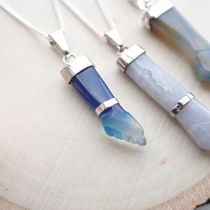 May include: Three silver necklaces with agate stone pendants. The pendants are carved into the shape of a hand. The stones are blue, white, and green.