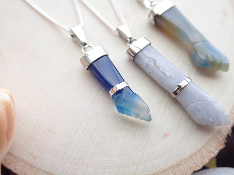 May include: Three silver necklaces with agate stone pendants. The pendants are carved into the shape of a hand. The stones are blue, white, and green.