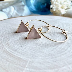 May include: Gold hoop earrings with a pink triangle pendant. The triangle is made of a translucent material with a slight shimmer.
