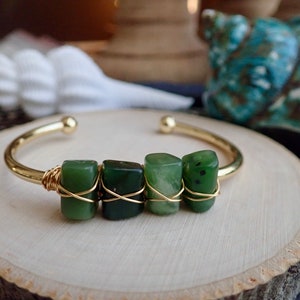 May include: A gold bangle bracelet with three green jade stones wrapped in gold wire.