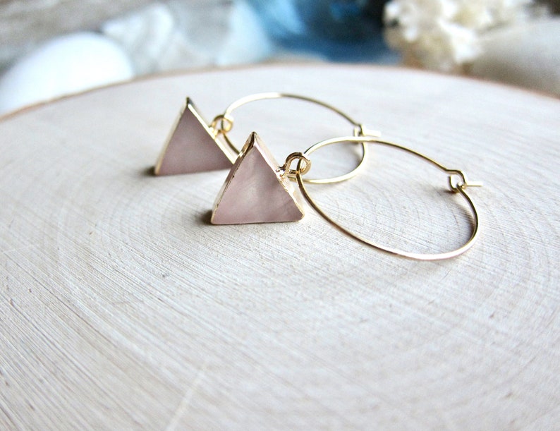 May include: A pair of gold hoop earrings with a pink triangle pendant on each hoop.