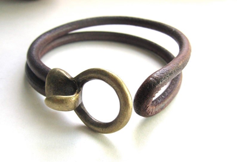May include: A brown leather bracelet with a brass clasp. The bracelet is double-layered and has a rustic look.