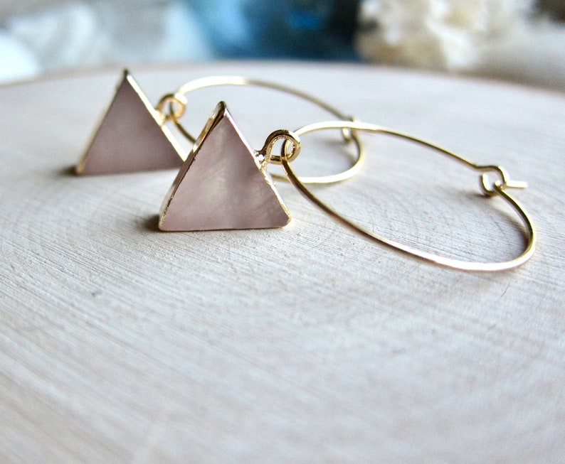 May include: Gold hoop earrings with a pink triangle pendant. The triangle is made of a pearlescent material.
