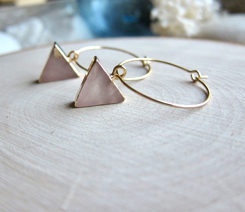 May include: Gold hoop earrings with a pink triangle pendant. The triangle is made of a pearlescent material.