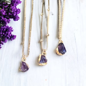 May include: Three gold chain necklaces with amethyst crystal pendants. Each pendant is a different shape and size, and has a gold-leaf finish.