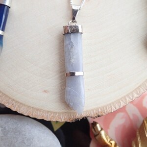 May include: A silver chain necklace with a light gray stone pendant. The pendant is shaped like a hand and has a silver band around the top.